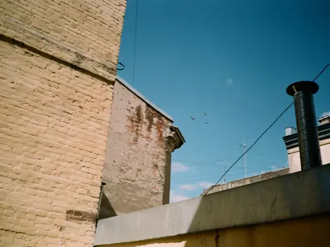 A rooftop vent pipe beside a brick wall under a blue sky