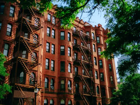 A sunlit brick apartment building with fire escapes