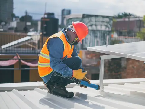 A roofer kneeling to work on a white metal roof