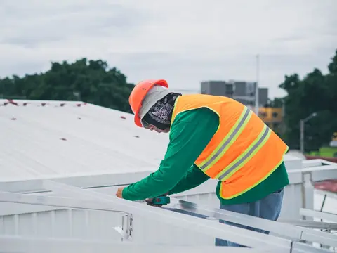 A roofer in a safety vest working on a white metal roof