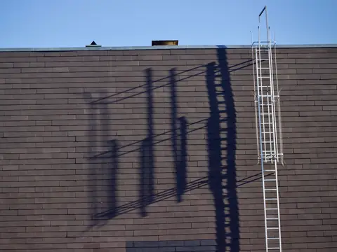 A roof-access ladder on a brick wall under a blue sky