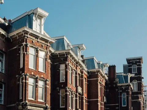 A row of brick houses with mansard roofs under a blue sky