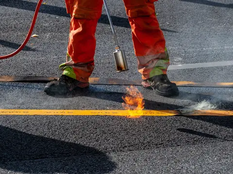 A roofer heating a new membrane with a torch on a flat roof