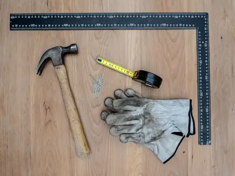 A hammer, square, tape and gloves laid out for a repair
