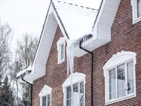 A brick house with snow on its roof and ice along the gutters
