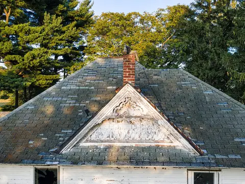 Worn shingles on an older pitched roof with a chimney
