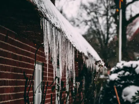 Icicles hanging from the snowy roof edge of a brick house