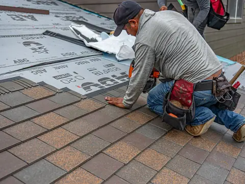 A roofer nailing new asphalt shingles over fresh underlayment