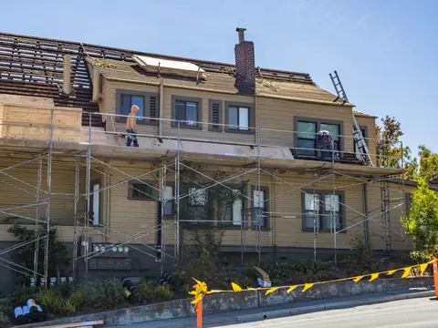 A two-story house under scaffolding while its roof is redone